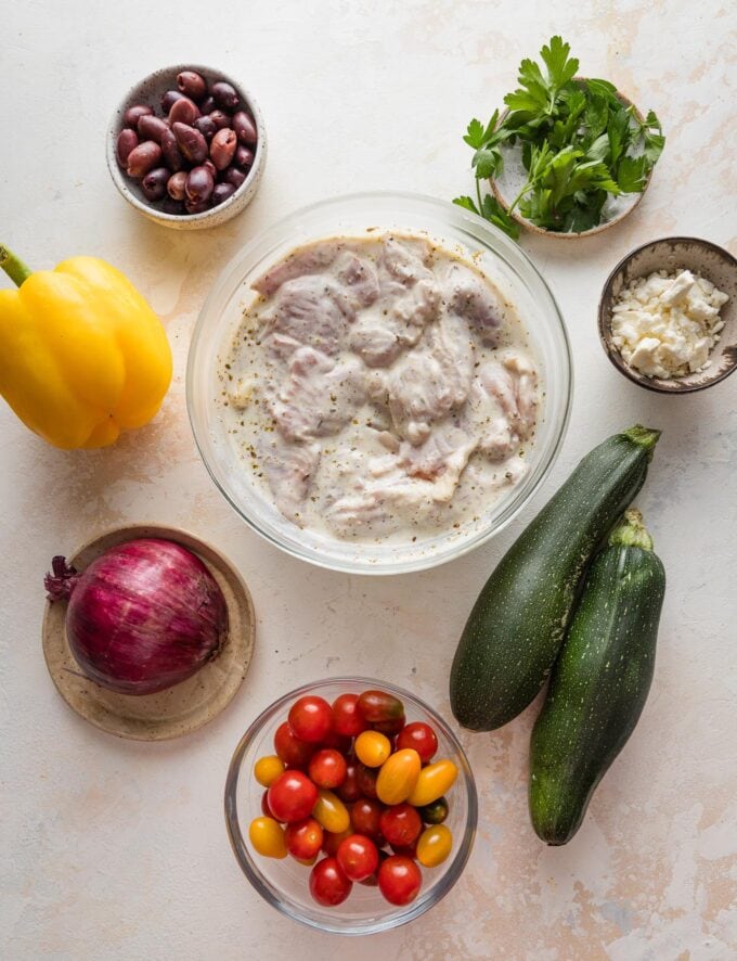 Ingredients for Greek chicken thighs and veggies (zucchini, tomatoes, red onion, bell pepper).