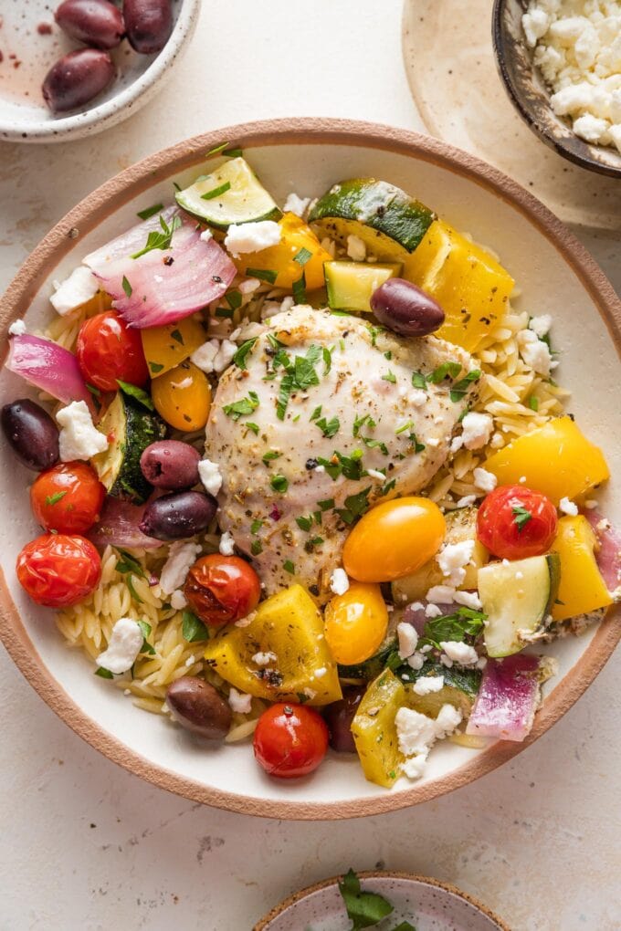 Bowl with couscous, roasted veggies, and a roasted Greek yogurt-marinated chicken thigh, sprinkled with olives, feta, and parsley.