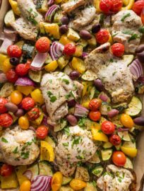 Sheet pan full of Greek yogurt-marinated chicken roasted with zucchini, tomatoes, red onion, and bell pepper.