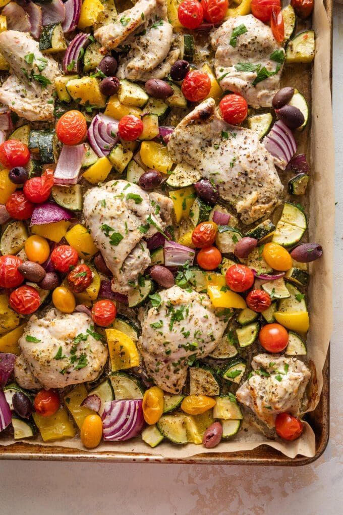 Sheet pan lined with parchment and filled with Greek chicken thighs and roasted veggies.
