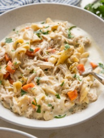 Angled view of a bowl full of one pot chicken and noodles with carrots and parsley.
