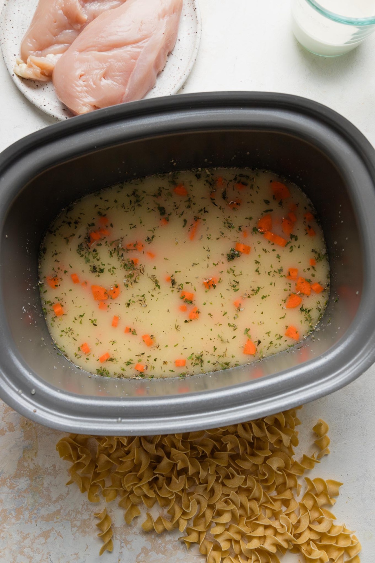Broth, carrots, and herbs mixed together in the bowl of a large slow cooker.