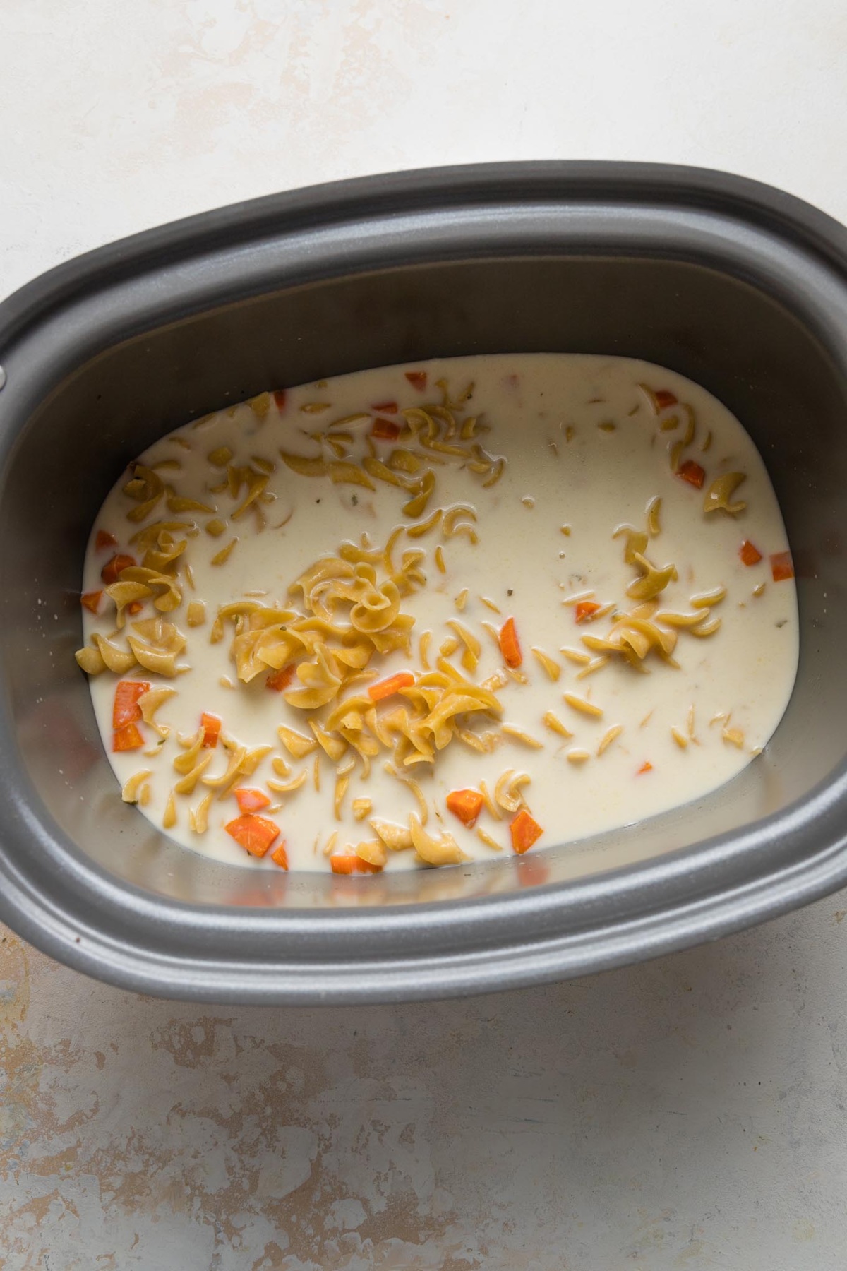 Egg noodles and a creamy broth mixture partially cooked in slow cooker.