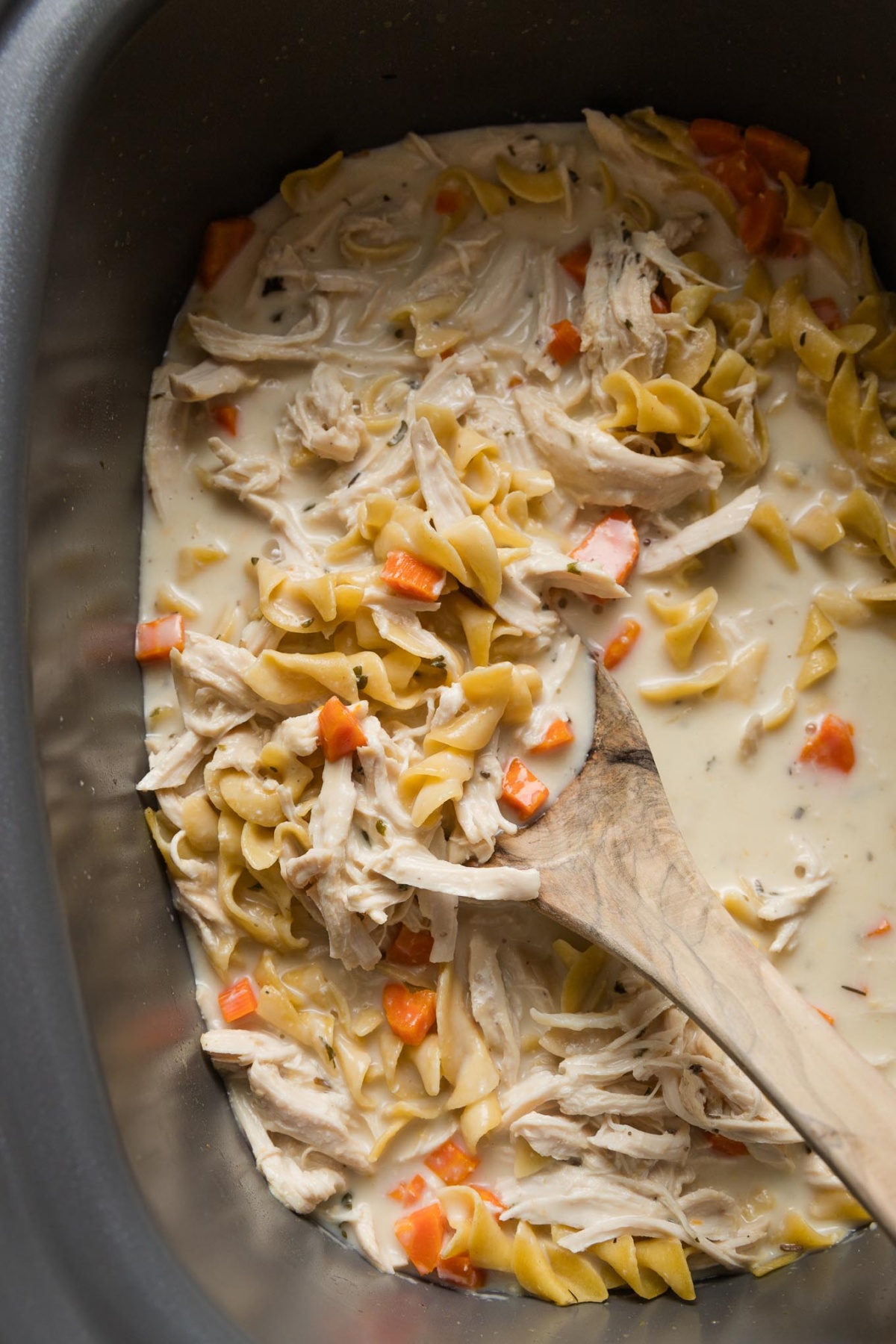 Wooden spoon stirring a finished dish of slow cooker chicken and noodles.