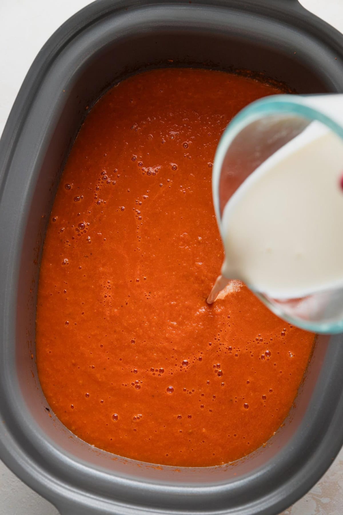 Heavy cream being poured into a slow cooker tomato soup.
