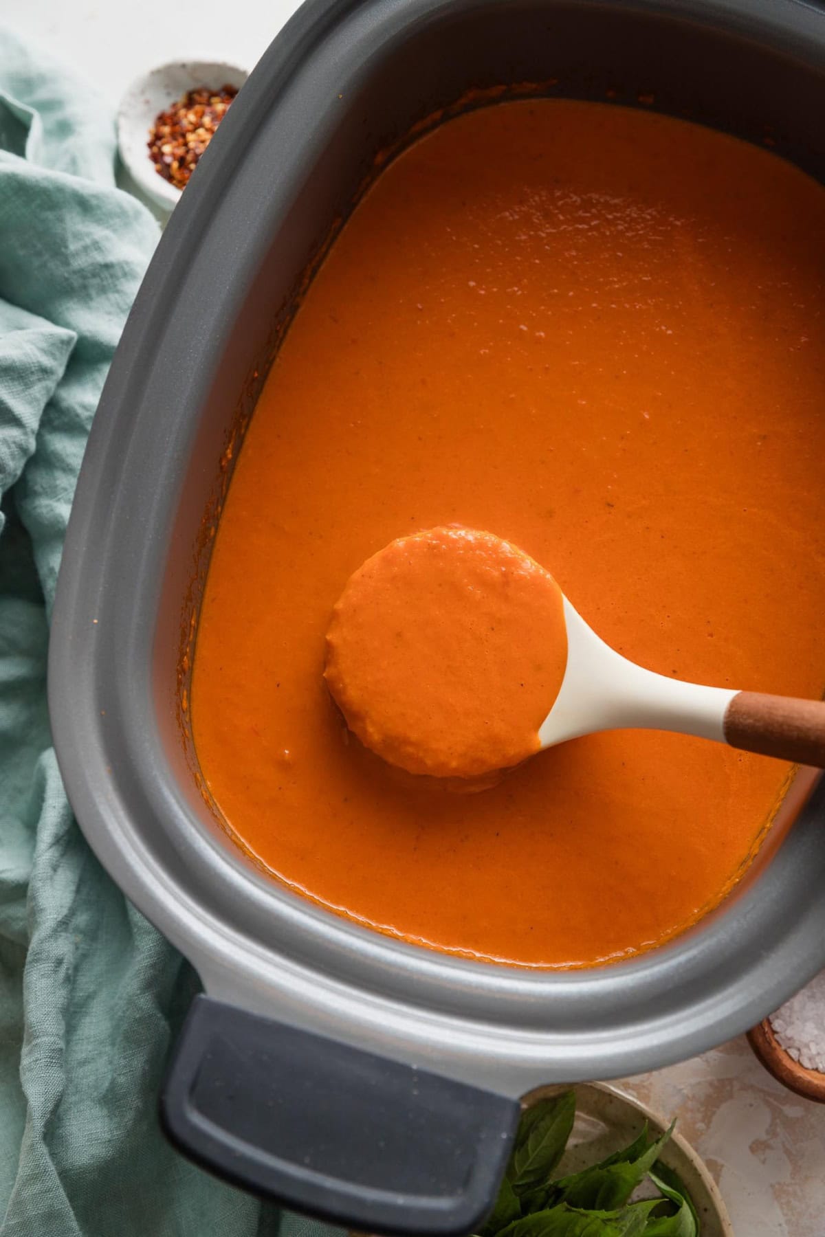 Ladle lifting out a spoonful of tomato soup from a Crockpot.