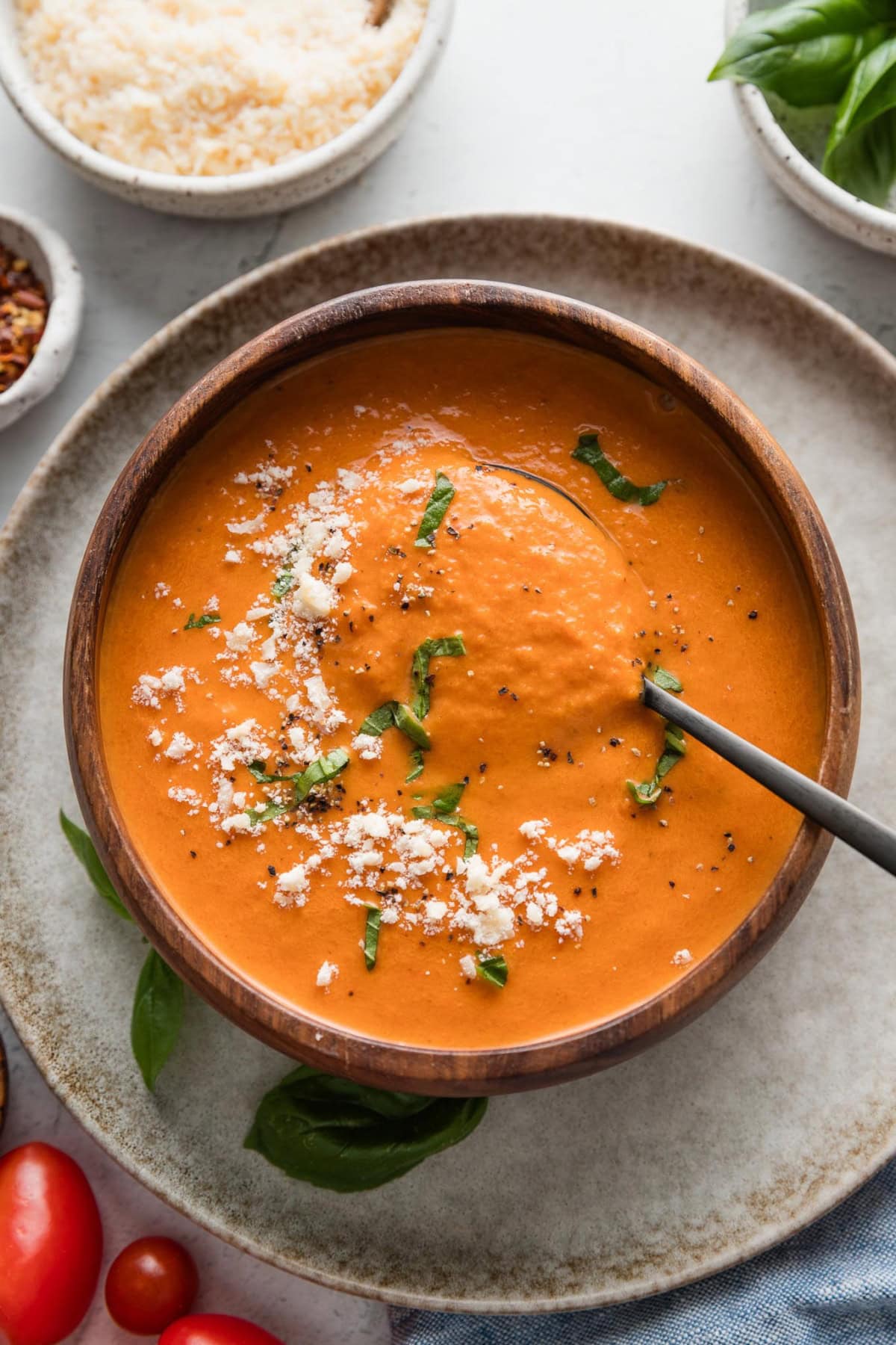 Spoon lifting up a bite of creamy tomato soup from a wooden bowl.