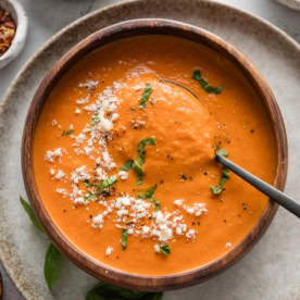 Spoon lifting up a bite of creamy tomato soup from a wooden bowl.