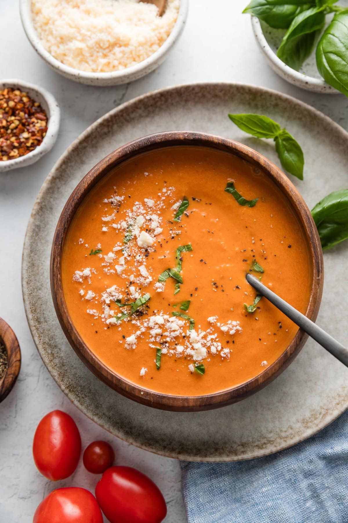 Wooden bowl filled with a cozy helping of tomato soup made in the slow cooker and topped with Parmesan cheese and fresh basil.