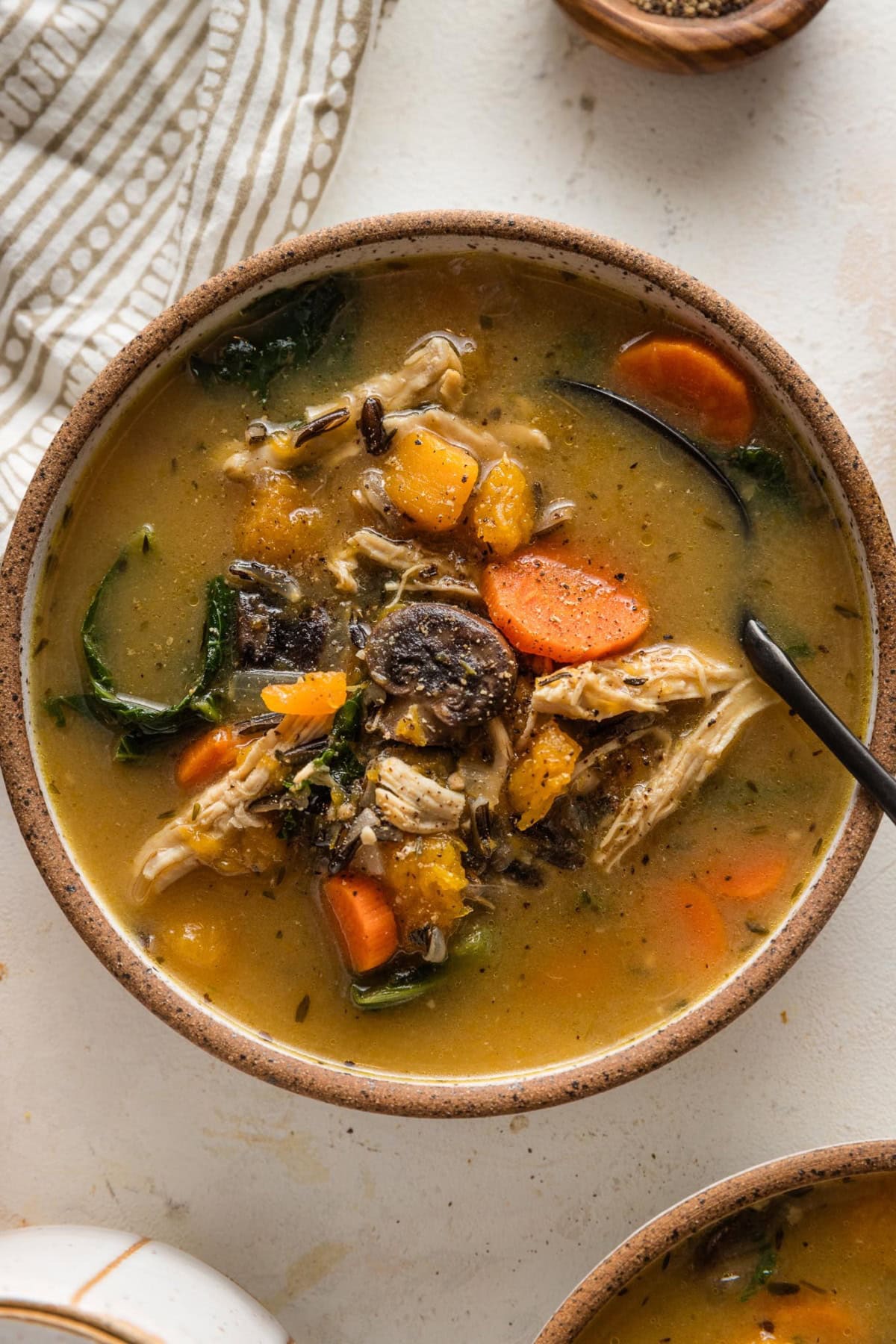 Wild rice soup with butternut and carrots and chicken in a small ceramic bowl.