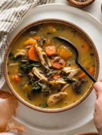 A small bowl full of soup with wild rice, chicken, butternut squash, carrots, and mushrooms.