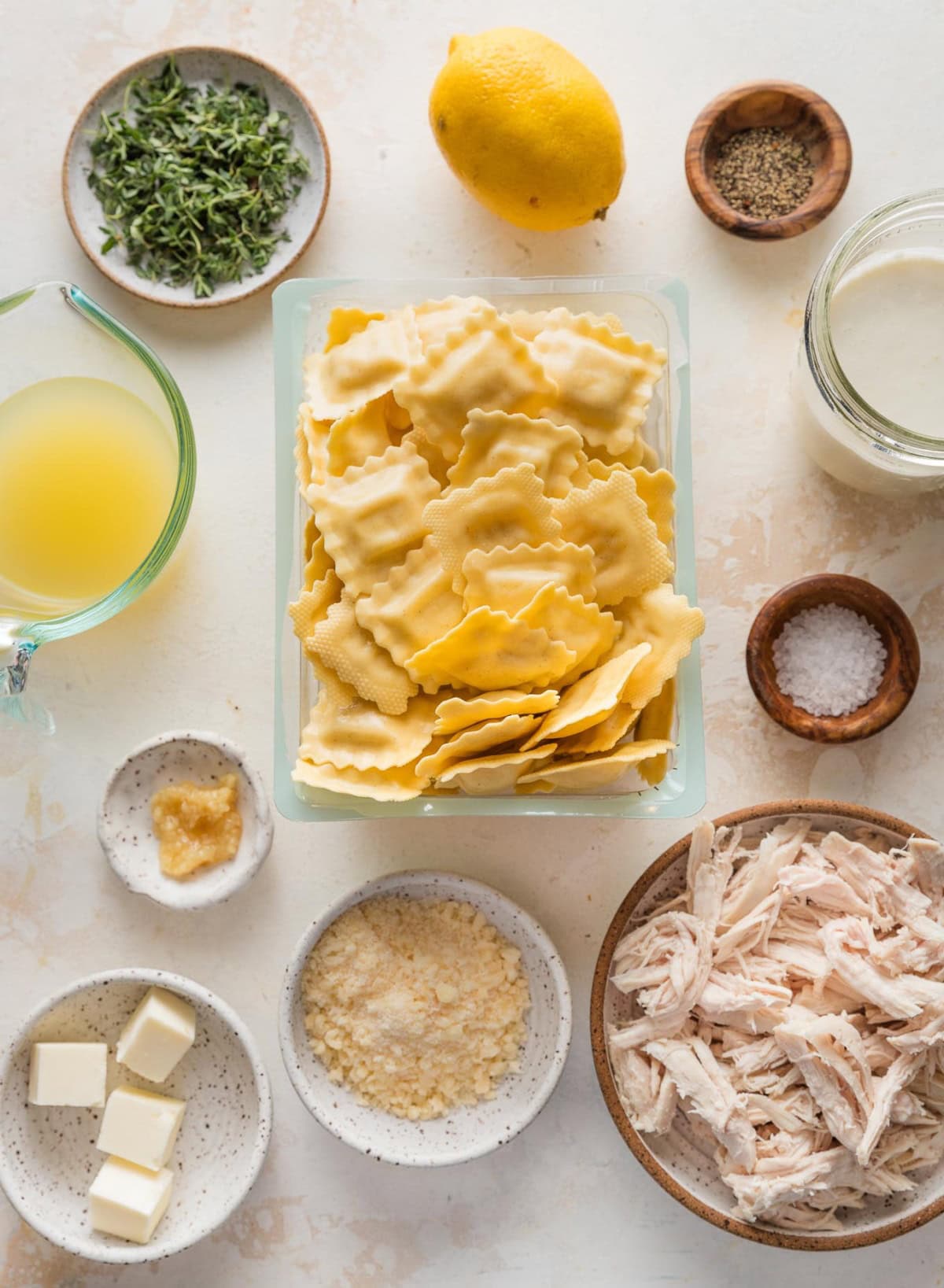 Overhead image of fresh cheese ravioli in their package, surrounded by fresh thyme, chicken broth, cream, shredded cooked chicken, garlic, butter, a whole lemon, salt, and pepper.