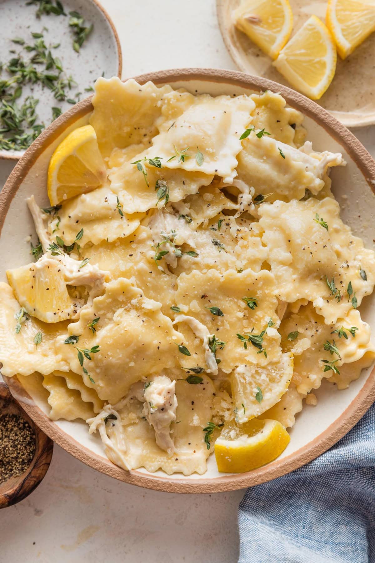 Bowl full of lemon chicken ravioli with a simple creamy garlic lemon pan sauce and extra lemon wedges and thyme.