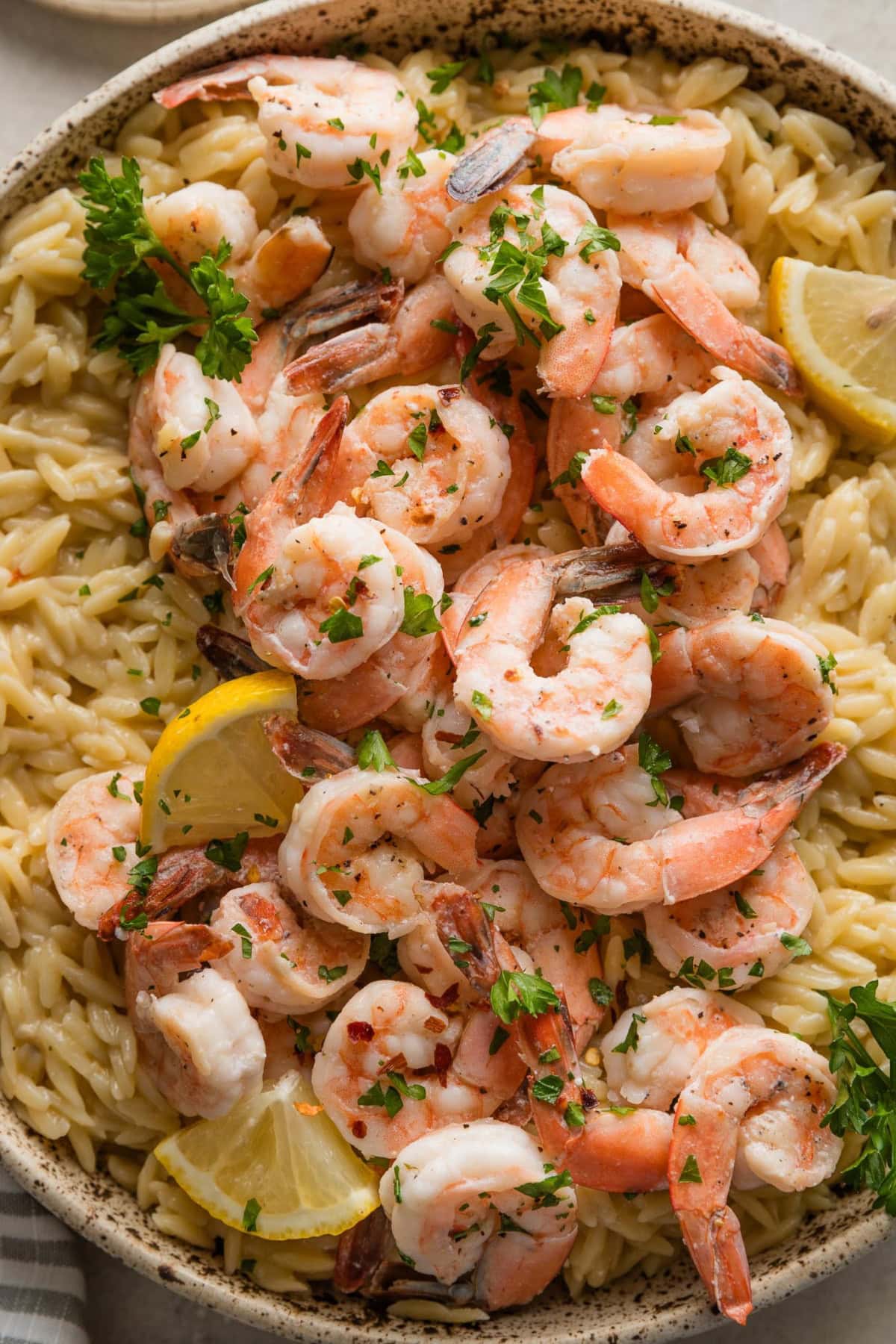 Close up of shrimp scampi orzo served in a beautiful speckled bowl with a garnish of lemon wedges and fresh parsley.
