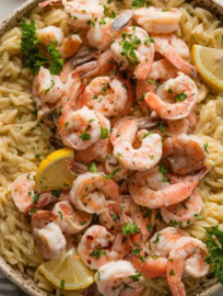 Close up of shrimp scampi orzo served in a beautiful speckled bowl with a garnish of lemon wedges and fresh parsley.