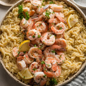 Speckled ceramic bowl filled with shrimp scampi topped with fresh parsley.