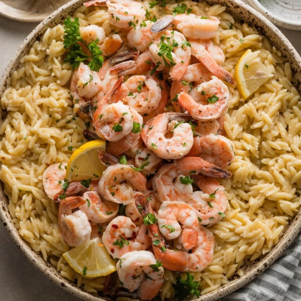 Speckled ceramic bowl filled with shrimp scampi topped with fresh parsley.