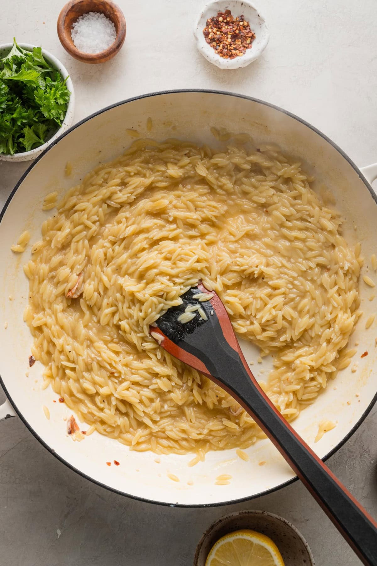 Spoon stirring orzo cooked in a skillet.