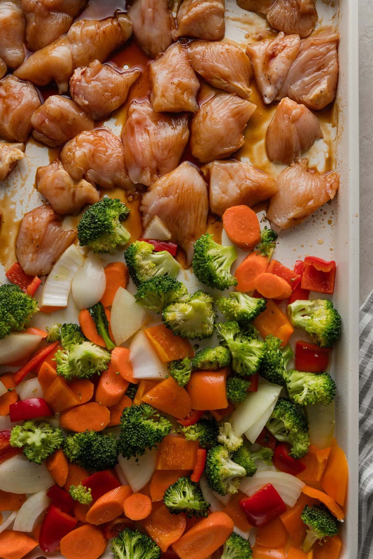 Raw bites of chicken tossed with teriyaki sauce added to a sheet pan with lots of colorful veggies.