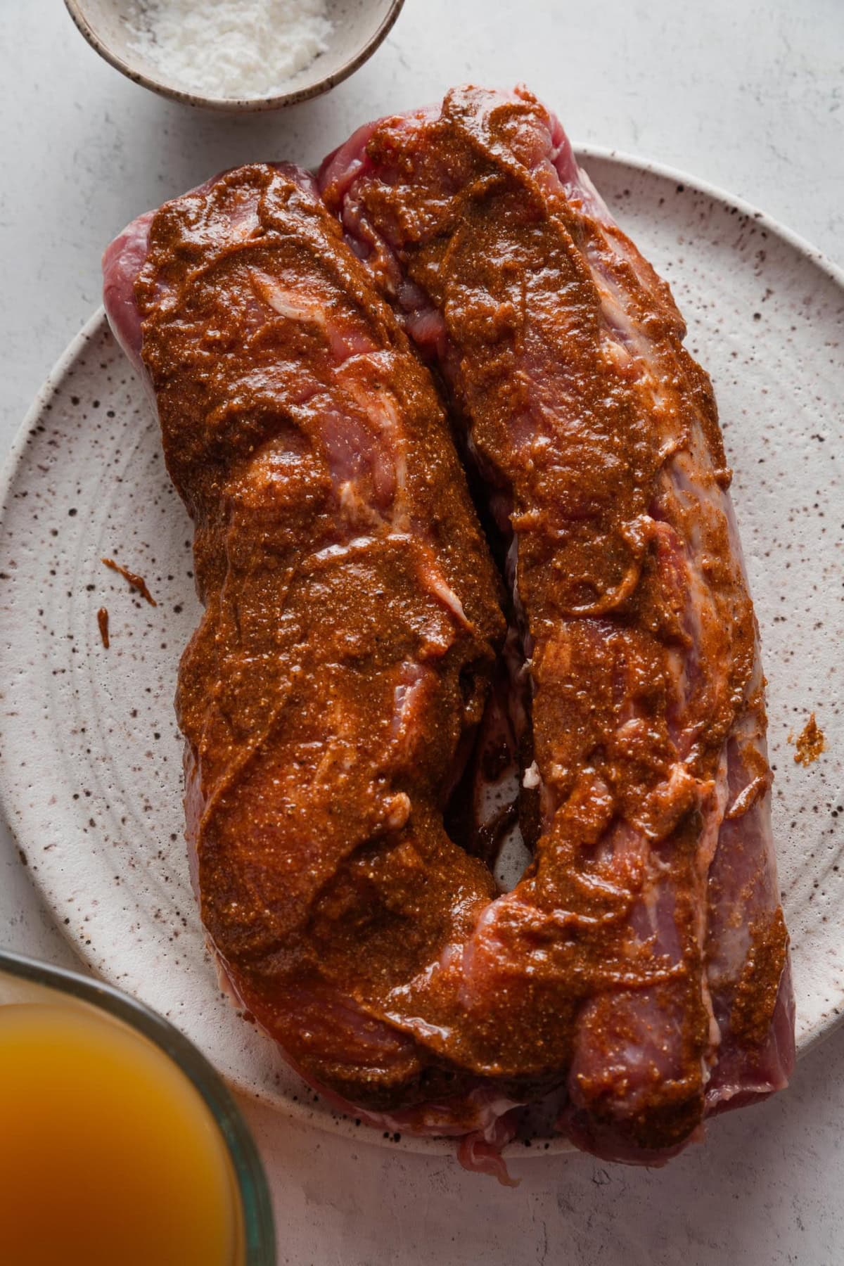 Two pork tenderloins covered in a seasoning rub and resting on a plate.