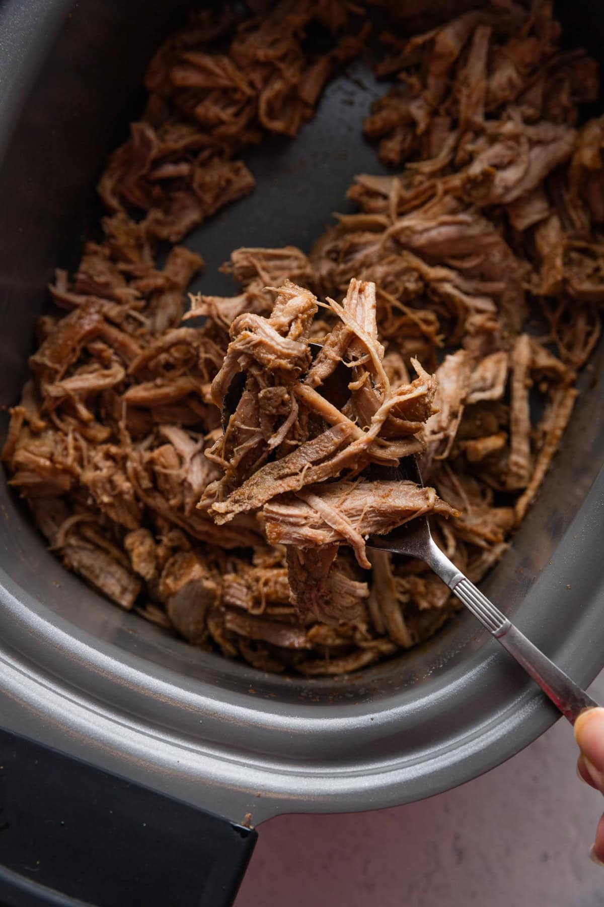 Close up of a serving spoon lifting pulled pork out of a large slow cooker.